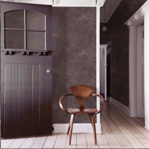 Entrance hall side wall with metallic concrete wallpaper smokey quartz installed. Also features passageway to the left, open fron door on right and modern wooden chair in foreground.