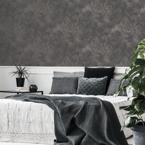 Bedroom with metallic concrete wallpaper quartz grey installed on the wall in the background. Foreground features a large white bed with dark throws and pillows