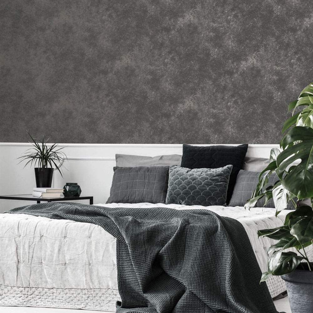 Bedroom with metallic concrete wallpaper quartz grey installed on the wall in the background. Foreground features a large white bed with dark throws and pillows