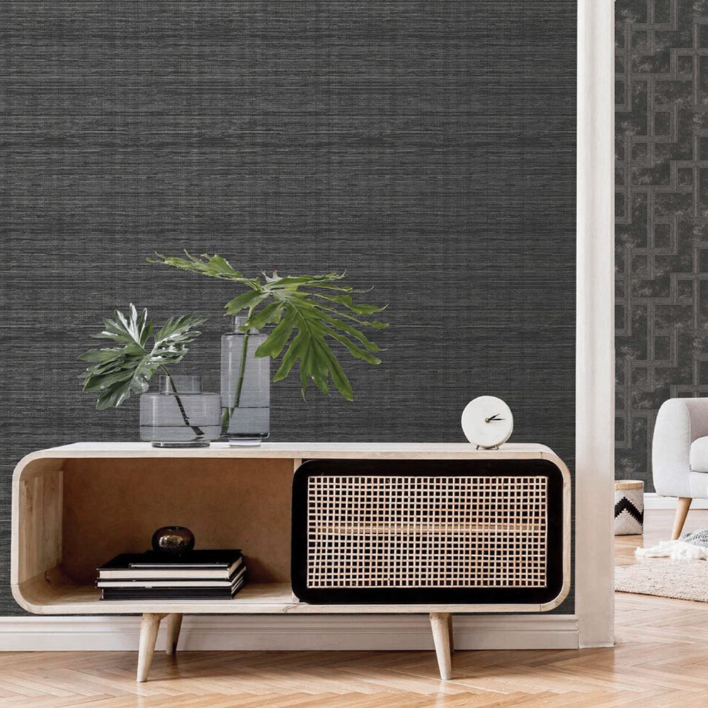 Lounge with Metallic Grasscloth Wallpaper Onyx Black installed on the wall. Also features a small sideboard with plant, desk clock and books.