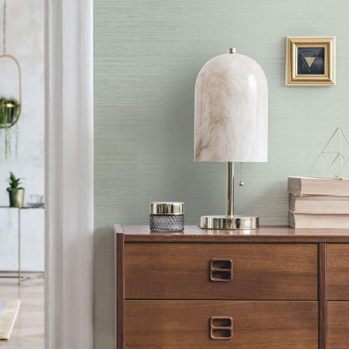 Entrance hall with the Metallic Grasscloth Wallpaper Sage installed on the wall. In fron of the wall is a sideboard holding a modern marble lamp, books and candles