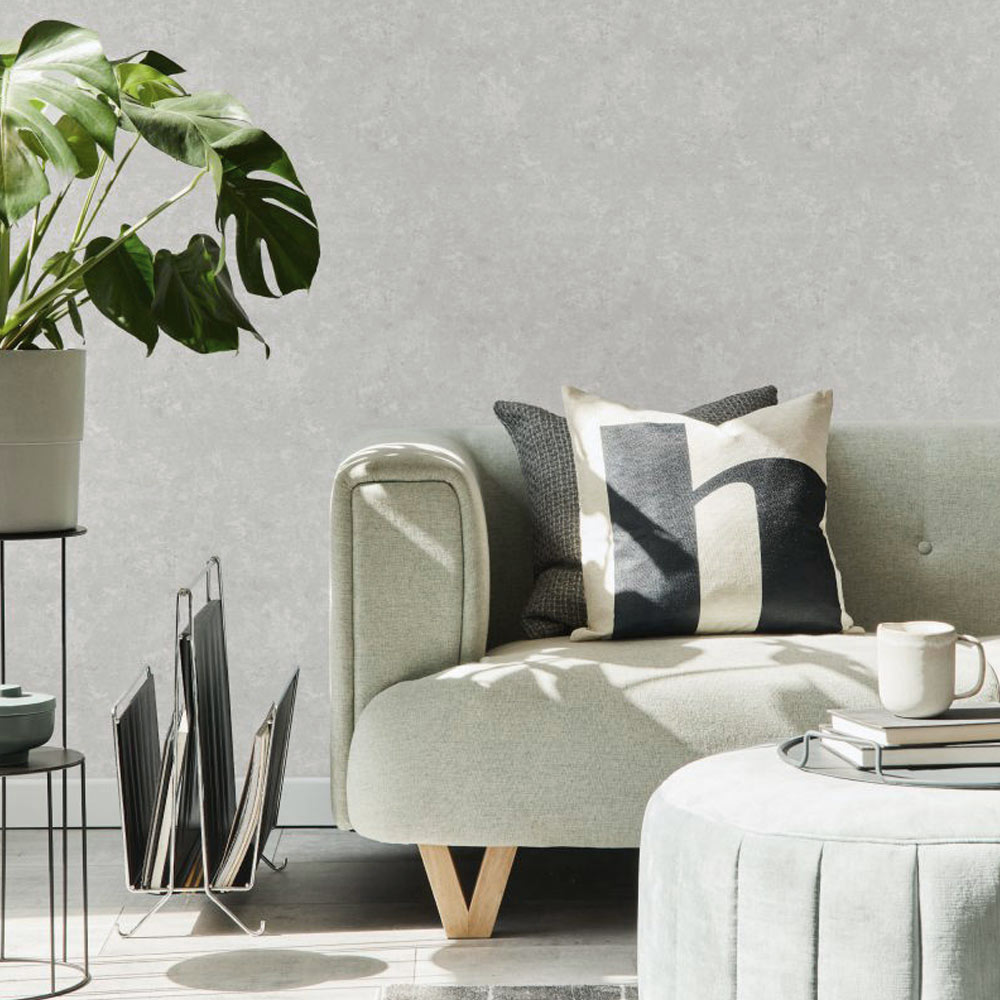 Lounge with Textured Plaster Wallpaper in Off White installed onto walls. The foreground contains a light sage green counch, ottoman table, plant on stand and magazine holder.