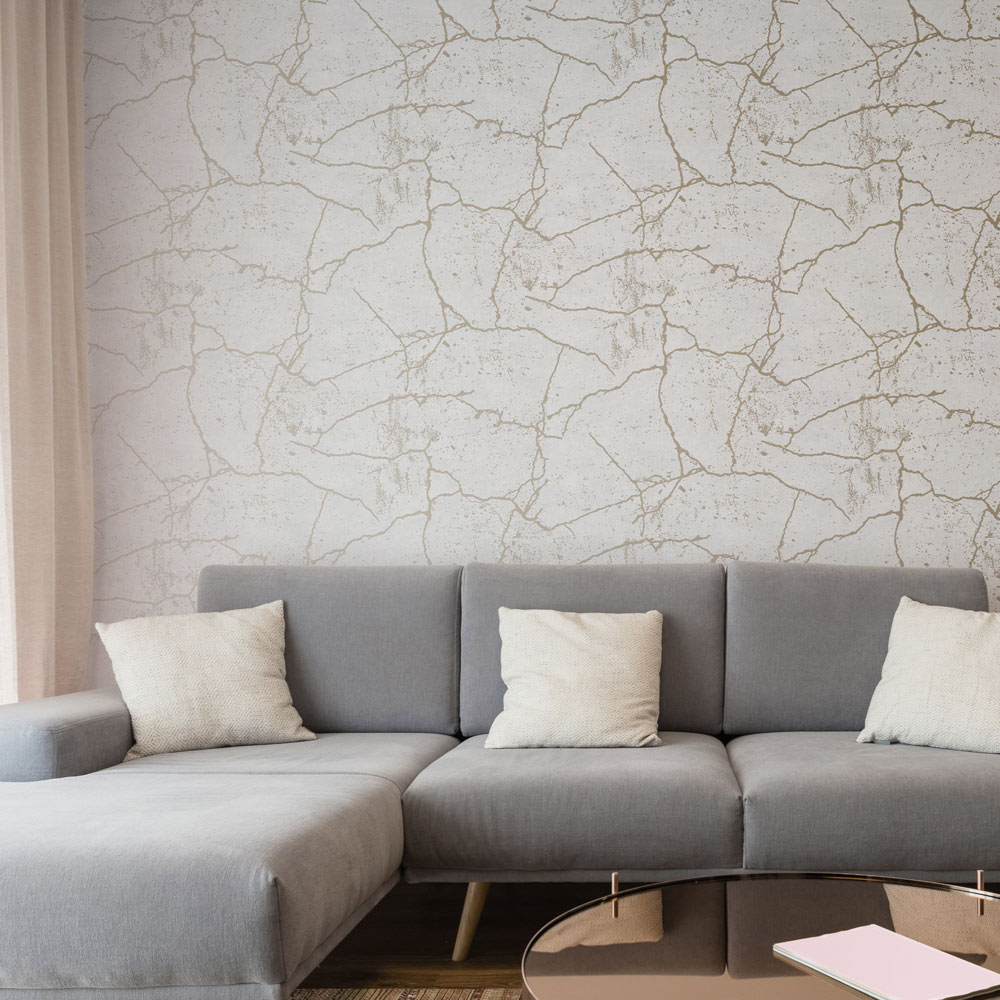 Lounge with Ivory white Concrete kintsugi gold wallpaper installed on the wall and grey L-shaped couch with pillows and metallic side table in the foreground