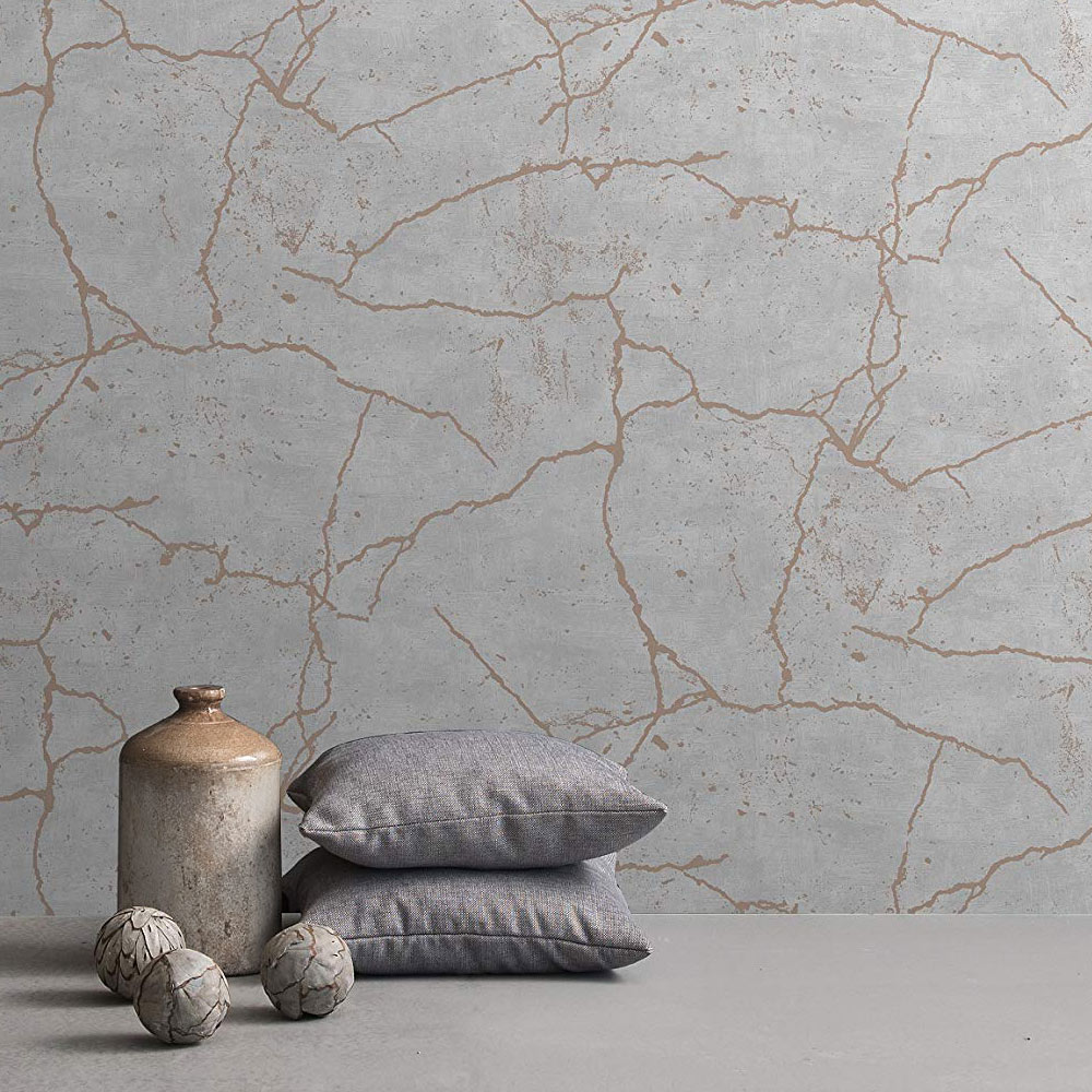 Detail shot of the wall with grey concrete wallpaper with rose gold on the wall. Foreground features cearmic bottle, 2 pillows and 3 small decor balls.