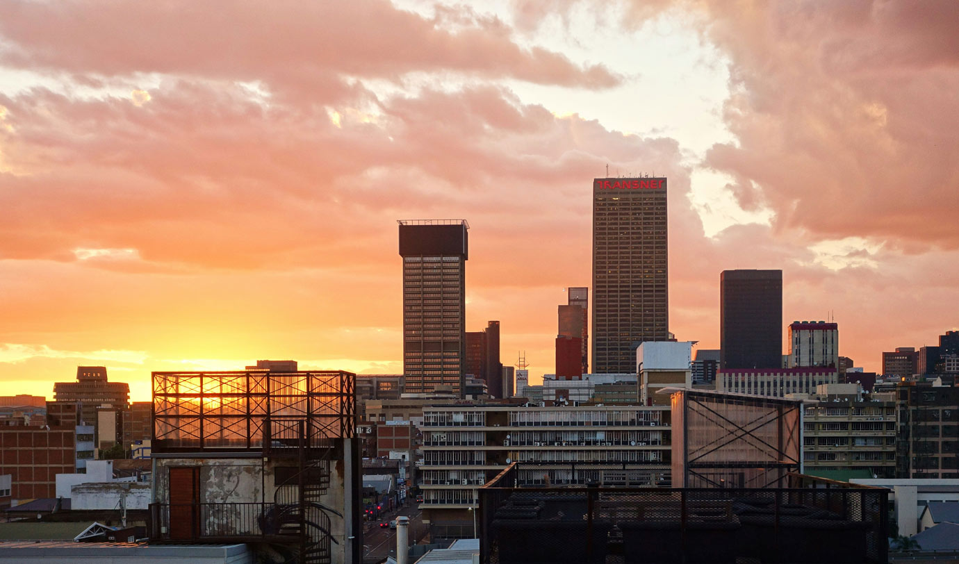 Skyline of Johannesburg duwing sunrise, silhouettes of buildings with orange red sky dotted with some clouds