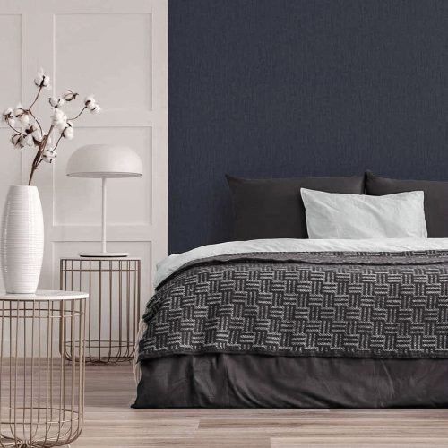 Bedroom with Metallic Draped Silk Wallpaper Sapphire Blue installed on the wall. Also features a large bed with pillows and thrown plus metal side table, modern lamp and a vase with cherry blossoms
