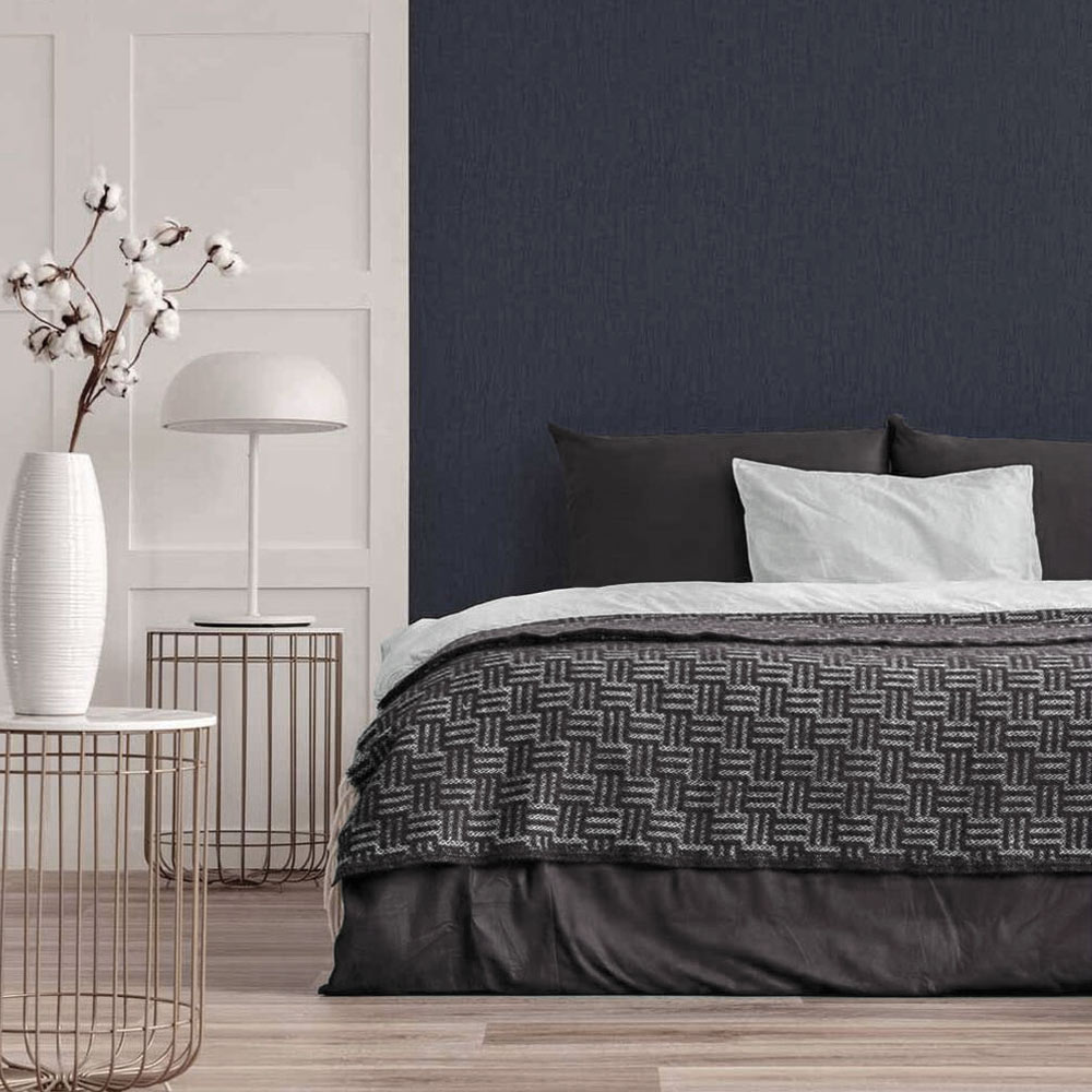 Bedroom with Metallic Draped Silk Wallpaper Sapphire Blue installed on the wall. Also features a large bed with pillows and thrown plus metal side table, modern lamp and a vase with cherry blossoms