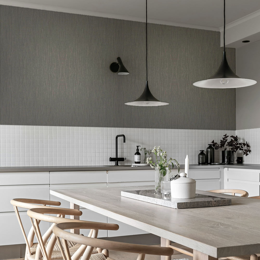 Kitchen with Metallic Draped Silk Wallpaper Smokey Quartz installed on the wall above white tiles. Kitchen also features black pendant lamps, black tap with sink and wooden table and chairs