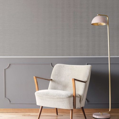 Waiting room with the metallic grasscloth wallpaper moonstone grey installed on the wall. Also features a simple standing lamp and a cream upholstered chair on wooden floor