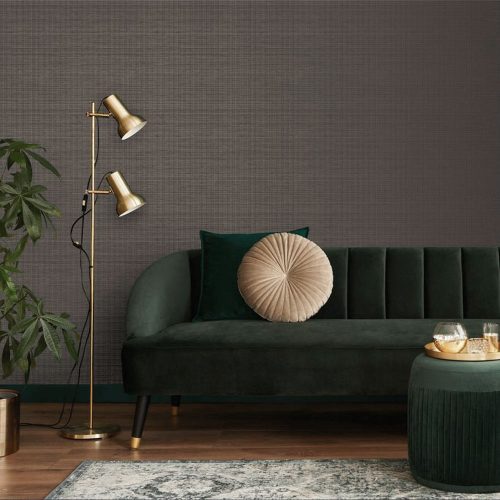 Longe with the metallic grasscloth wallpaper taupe installed on the wall. Also shown is a gold standing lamp, leafy plant and green velvet couch with cream round pillow and green velvet ottoman