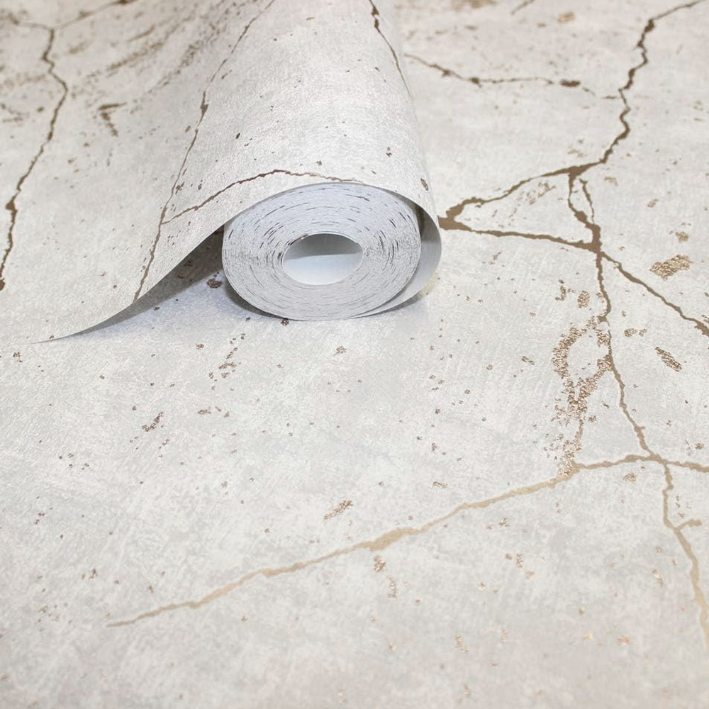 Close up of a roll of white and gold wallpaper showing textured cracked plaster effect