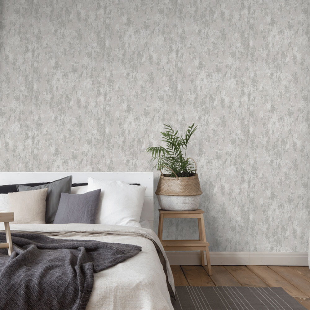 Bedroom with Weathered Concrete Wallpaper Silver Grey installed on the wall. Also featured double bed in white with grey thrown and pillows, side table with small potted palm.
