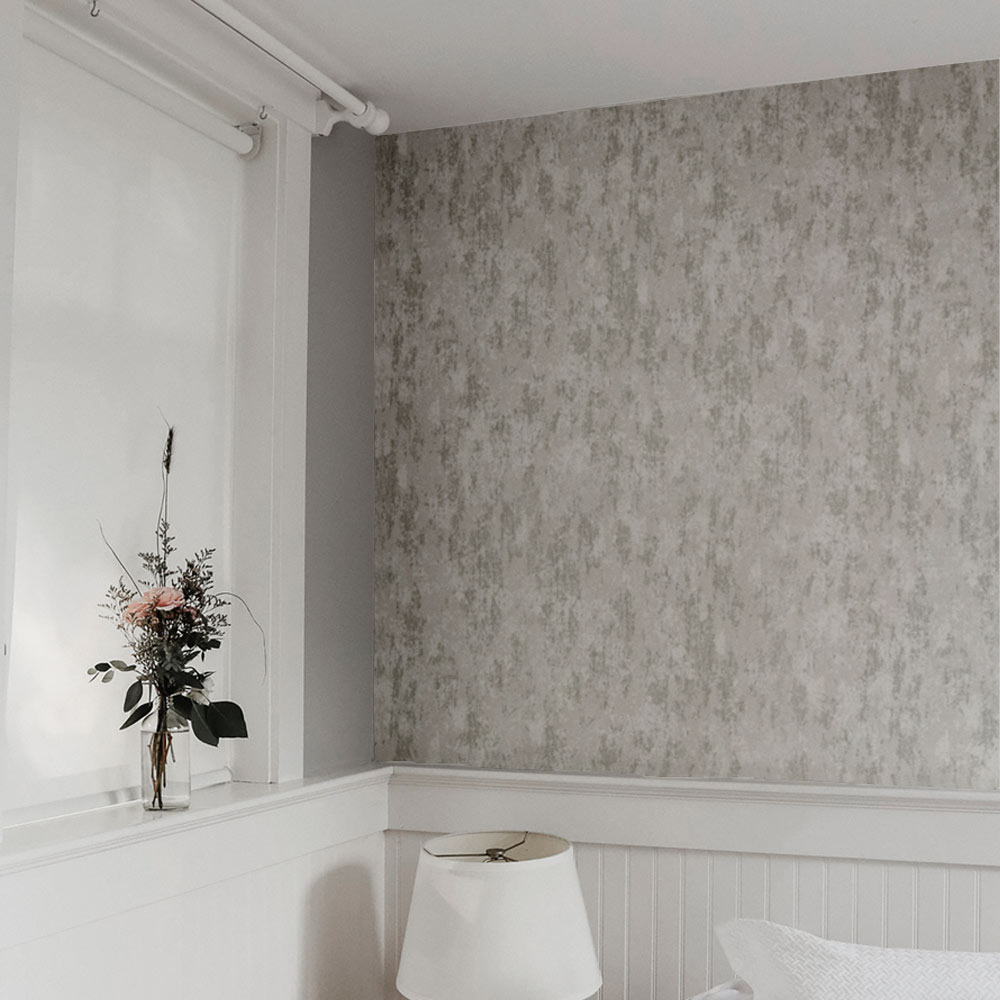 Bedroom with grey distressed industrial concrete effect wallpaper installed on the wall. Also features a cropped bed with pillows, bed lamp plus window with net curtains and a vase with a rose