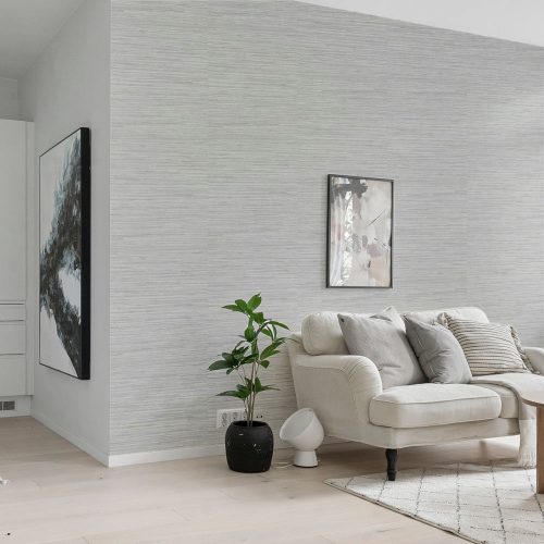Lounge with woven grasscloth wallpaper installed on the wall. Also features modern art on the wall, a couch, mat, coffee table and pot plant