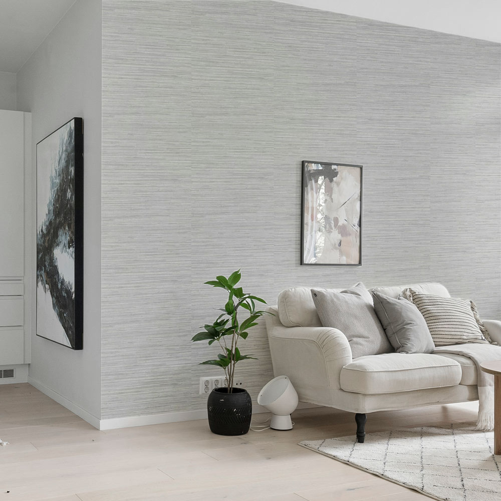 Lounge with woven grasscloth wallpaper installed on the wall. Also features modern art on the wall, a couch, mat, coffee table and pot plant